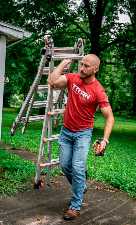 A Titan Roofing crew member carrying a ladder to a job