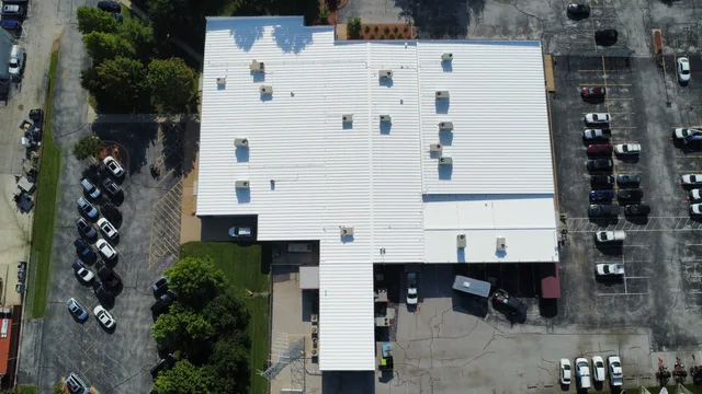 Aerial view of a large commercial building with a new white standing-seam metal roof, parking on three sides
