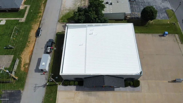 Aerial view of a commercial building with a new white metal roof beside its parking lot