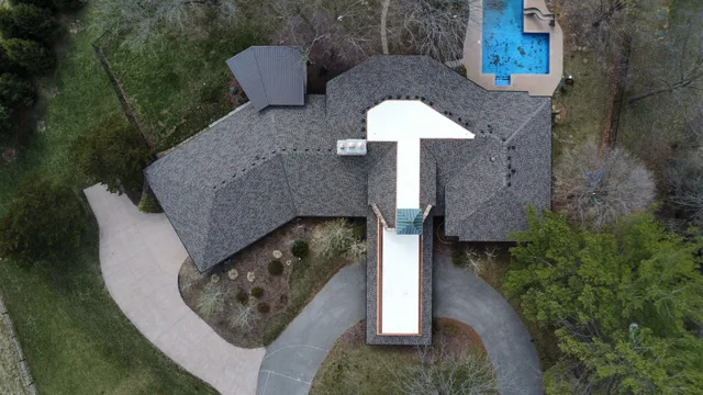 Aerial view of a home with a new charcoal shingle roof and white membrane over its flat sections