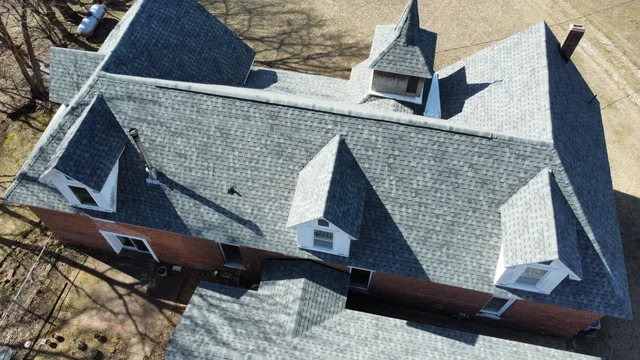 Aerial view of a brick farmhouse with a new weathered-grey shingle roof and dormer windows