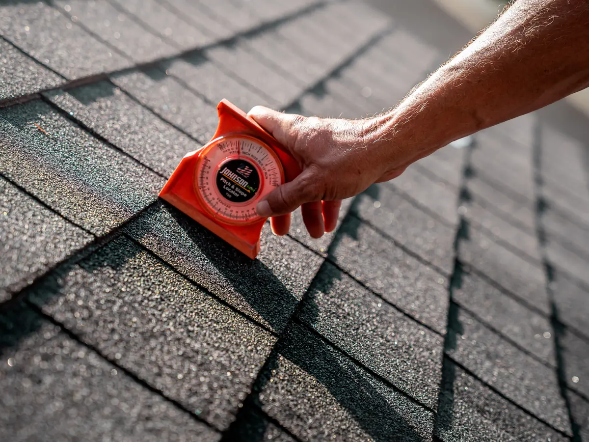 Pitch gauge held against an asphalt shingle roof during an inspection