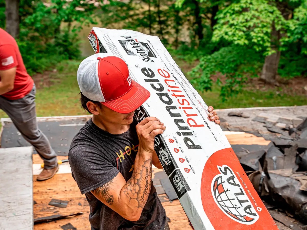 Crew member carrying a bundle of Atlas Pinnacle Pristine shingles across a roof deck
