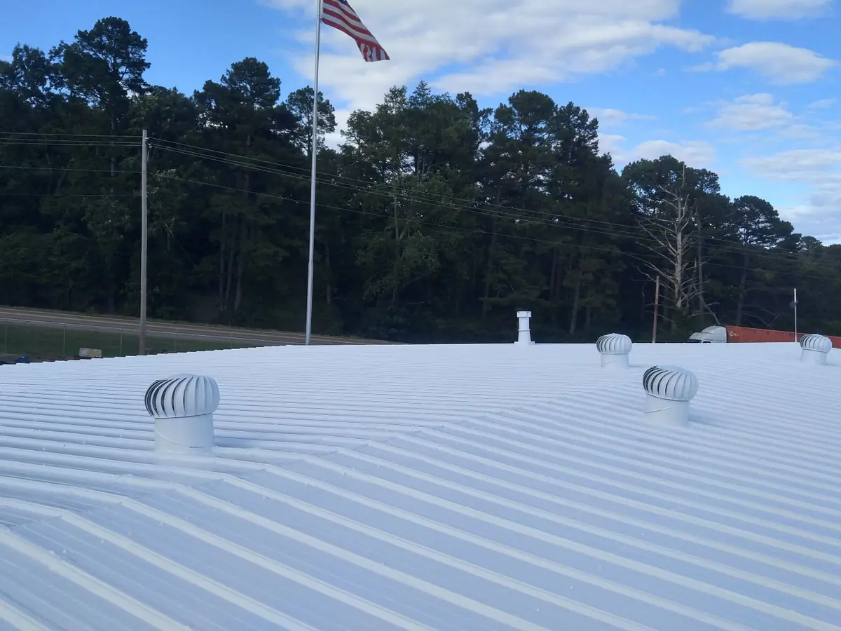 White coated metal roof on a commercial building with vents and a flagpole