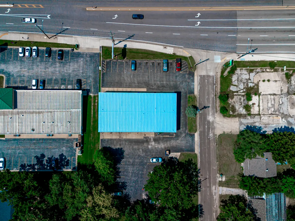 Two commercial roofs seen from directly above, one freshly coated blue and one older dark roof