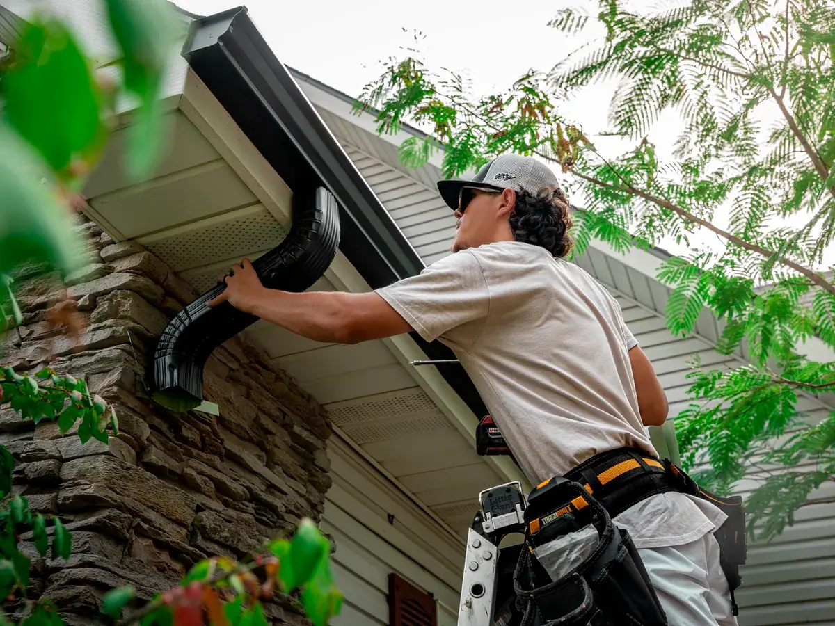 Titan Roofing installer fitting a black downspout elbow under a new seamless gutter
