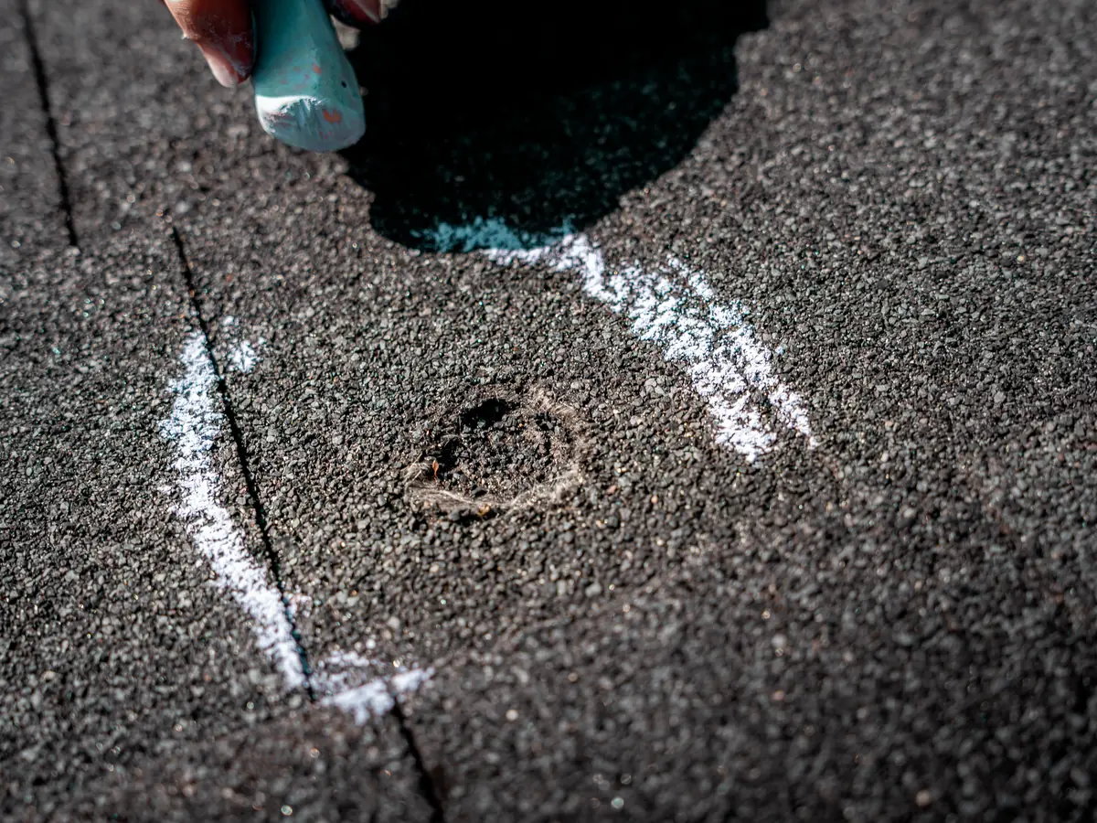 Chalk circle around a hail bruise on an asphalt shingle