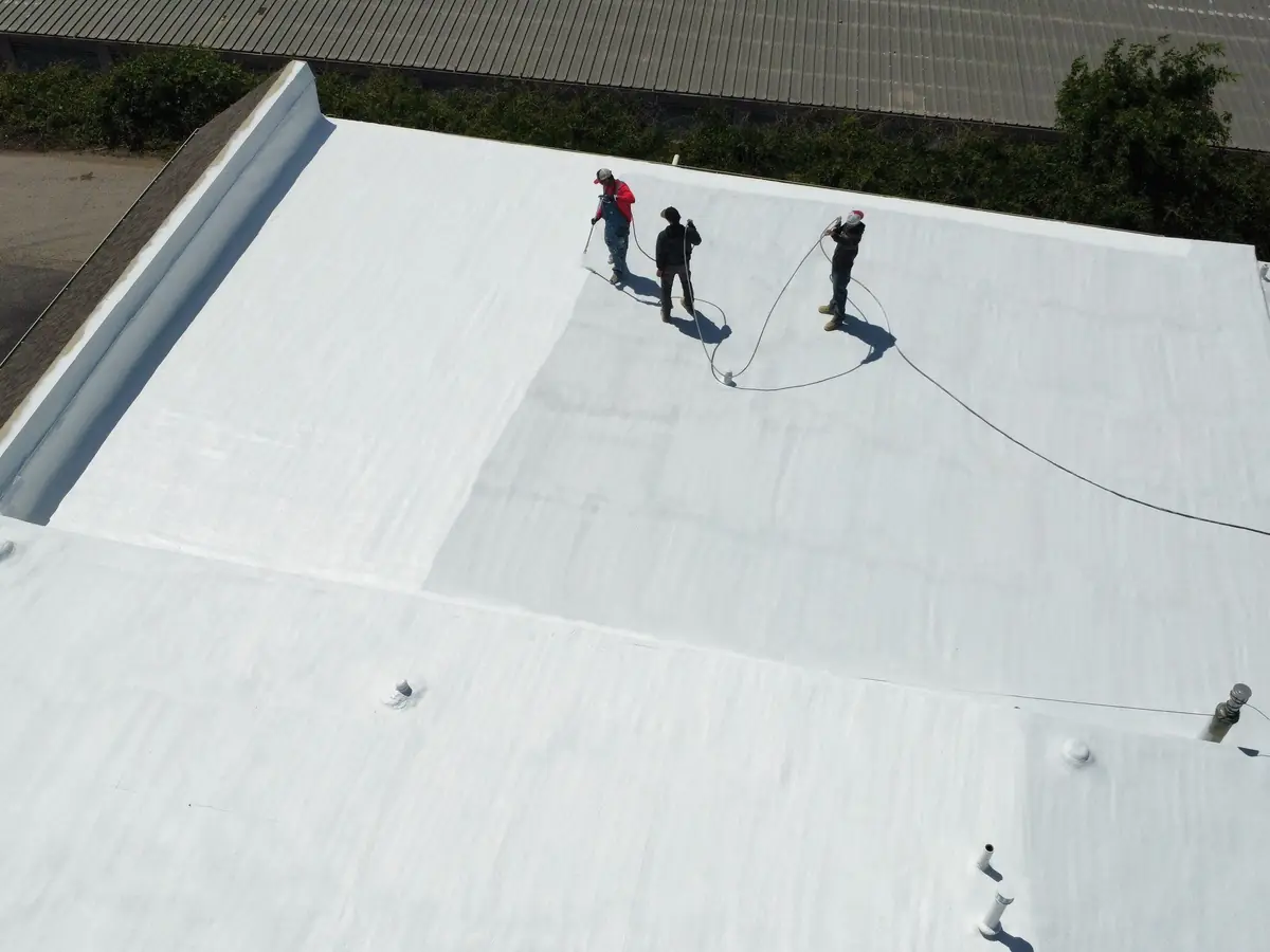 Wide commercial roof being coated over spray foam by a Titan crew
