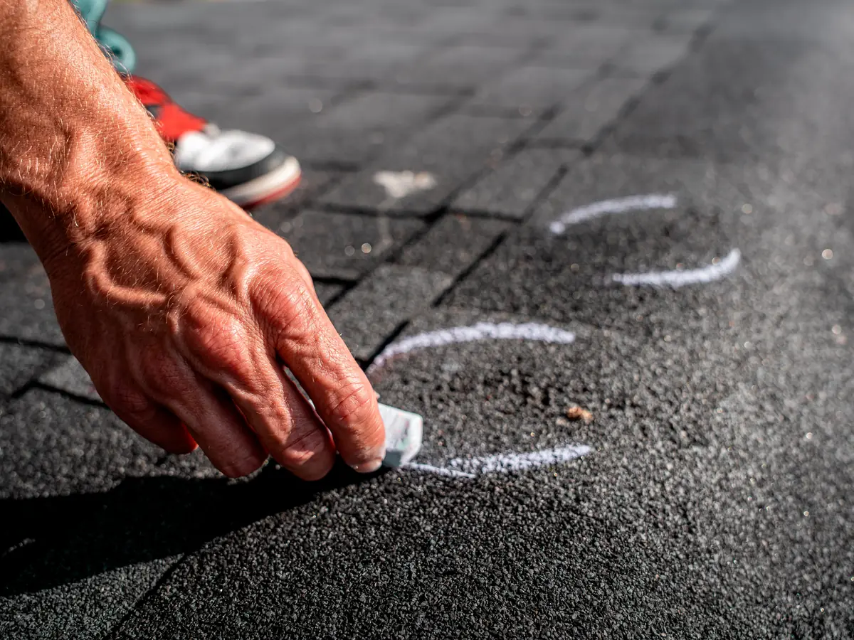 Hand marking hail damage on a shingle roof with chalk