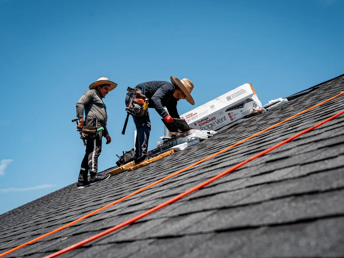 Titan Roofing crew installing shingles on a steep roof under a blue sky