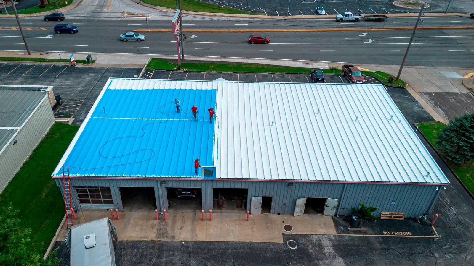 Titan crew finishing a bright blue roof coating on a commercial metal building, seen from above