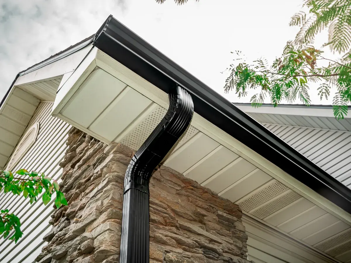 New black seamless gutter and downspout on the stone corner of a Missouri home, installed by Titan Roofing