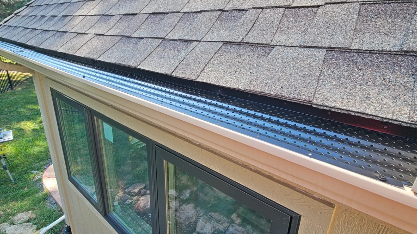 Gutter guards installed over a new gutter run along a shingle roof