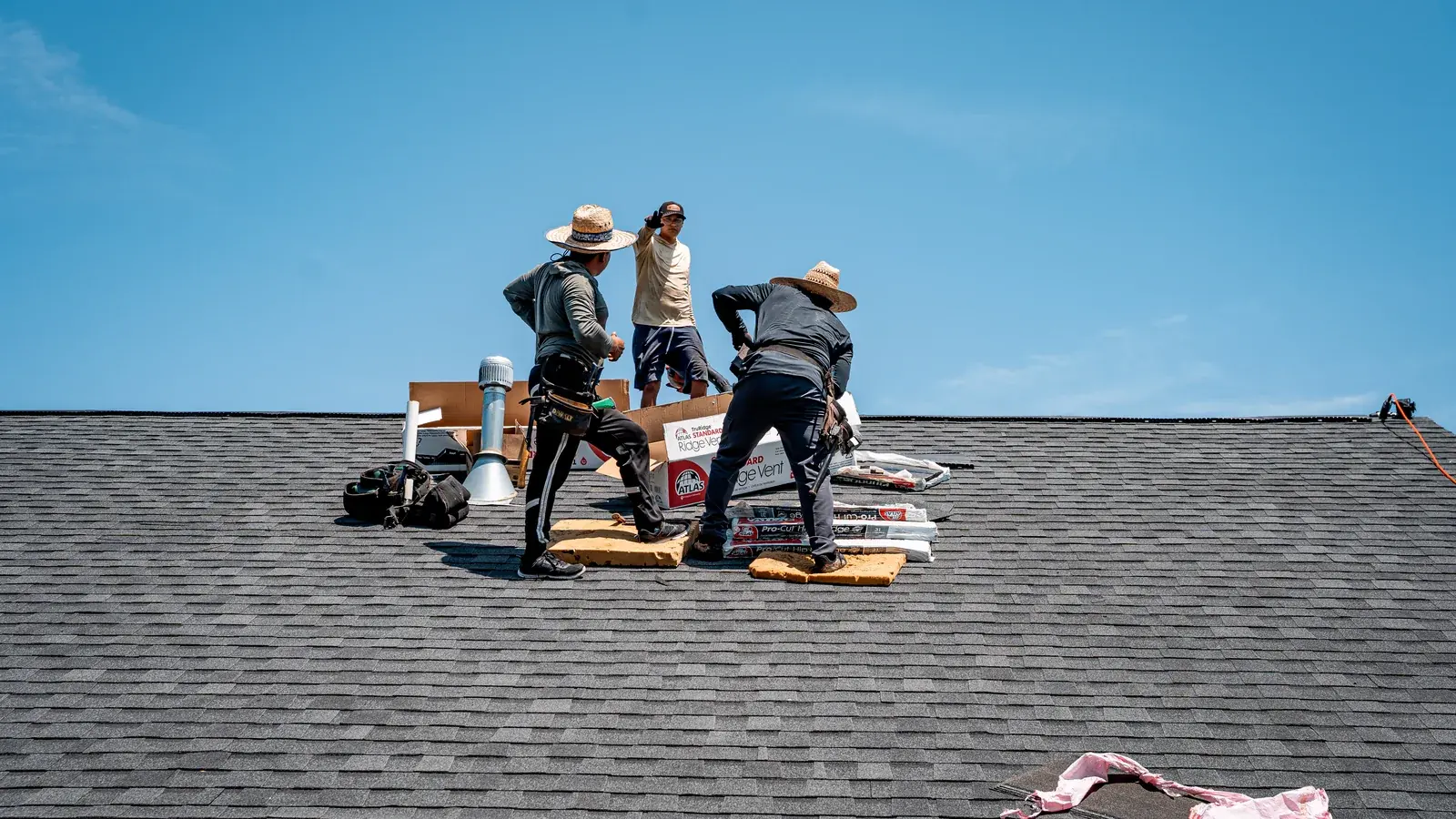 Roofing crew finishing the ridge of a new shingle roof under a blue sky