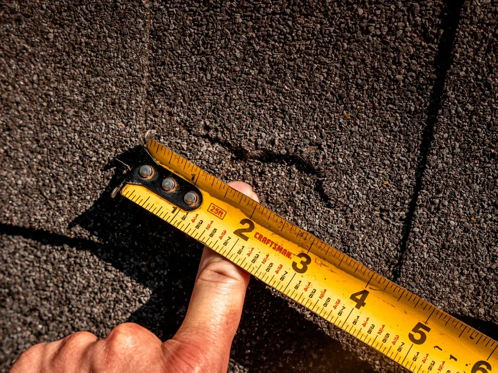 Titan inspector measuring a damaged area of a shingle roof